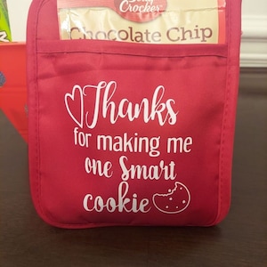 May include: Red oven mitt with a pocket that has a package of Betty Crocker chocolate chip cookie mix inside. The oven mitt has white text that says "Thanks for making me one smart cookie" with a heart and a cookie graphic.