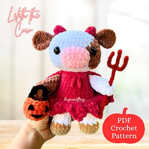 May include: A crocheted cow doll with brown, white, and pink details, wearing a red dress and holding a red pitchfork and a jack-o'-lantern. The text "Lifth the Cow" and "PDF Crochet Pattern" are visible.