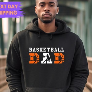 May include: Black basketball dad hoodie.  The text 'BASKETBALL DAD' is displayed in large, bold, white letters. The letters 'D' and 'A' are incorporated with orange basketball graphics. Next Day Shipping is mentioned.
