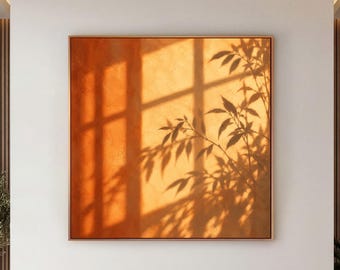 May include: A large square wall art piece featuring a vibrant orange background with a dark silhouette of bamboo leaves and window frame shadows cast across the surface, framed in a thin metallic border centered on a white wall.