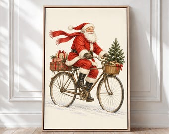 May include: A framed wall art print depicting Santa Claus riding a vintage bicycle through the snow. Santa wears a red suit with white fur trim and a long red scarf. A basket on the handlebars holds a small pine tree, and wrapped gifts are on the rear rack.