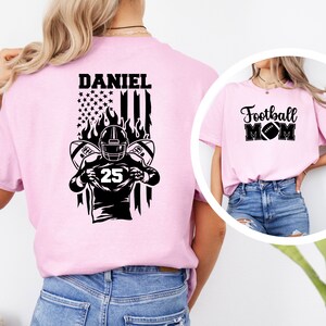 May include: Pink t-shirt with a black and white design of a football player with the text "DANIEL" and a US flag. A second pink t-shirt with the text "Football MOM" and a football graphic.