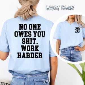 May include: Light blue t-shirts with black text. One shirt has the text "NO ONE OWES YOU SHIT. WORK HARDER" on the back. Another shirt has a skull graphic and the text "NOBODY CARES. WORK HARDER".