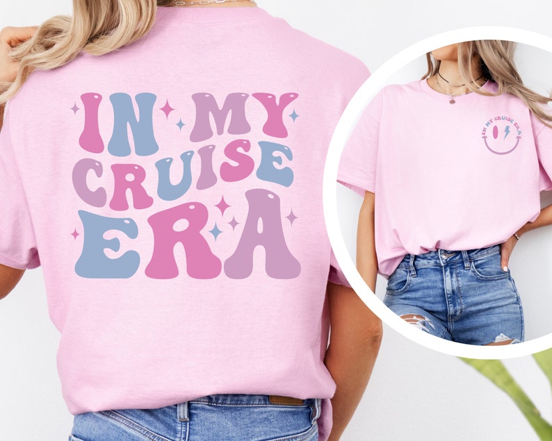 Puede incluir: Camiseta rosa con el texto "In My Cruise Era" en fuente retro azul y rosa con estrellas. La parte posterior de la camiseta tiene una carita sonriente rosa y azul con un rayo.