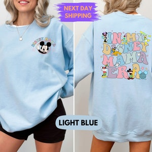 May include: Light blue sweatshirt with a Mickey Mouse graphic on the front and the text "In My Disney Mama Era" with various Disney characters on the back.