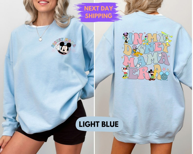 May include: Light blue sweatshirt with a Mickey Mouse graphic on the front and the text "In My Disney Mama Era" with various Disney characters on the back.
