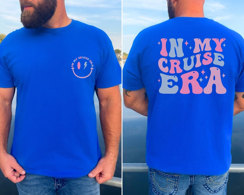 Puede incluir: Una camiseta azul real con una carita sonriente rosa y blanca con un rayo en la parte delantera y el texto "IN MY CRUISE ERA" en rosa y gris en la parte trasera.