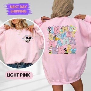 May include: Light pink sweatshirt with a Mickey Mouse graphic on the front and "In My Disney Mama Era" text with Disney characters on the back.