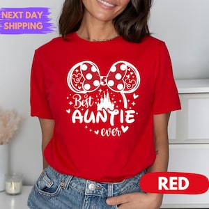 Puede incluir: Camiseta roja con un gr&aacute;fico blanco que presenta un lazo de lunares, un castillo y el texto "Best Auntie ever". La camiseta tiene mangas cortas y cuello redondo. La palabra "RED" se muestra en un &oacute;valo rojo.
