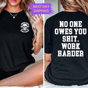 May include: Black t-shirt with white text and graphics. The front features a skull with crossed wrenches and the words "NOBODY CARES WORK HARDER". The back displays "NO ONE OWES YOU SHIT. WORK HARDER" in bold, block letters.