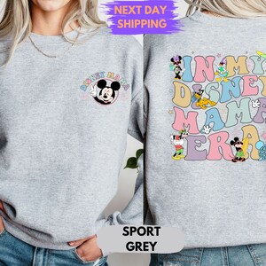 May include: A gray sweatshirt with a Mickey Mouse graphic on the front and the text "In My Disney Mama Era" with various Disney characters on the back. The sweatshirt is available in sport gray.