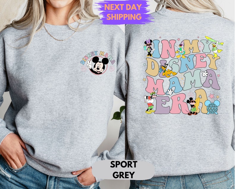 May include: A gray sweatshirt with a Mickey Mouse graphic on the front and the text "In My Disney Mama Era" with various Disney characters on the back. The sweatshirt is available in sport gray.