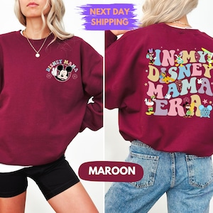 May include: A maroon sweatshirt with a Mickey Mouse graphic on the front and the text "In My Disney Mama Era" with various Disney characters on the back.