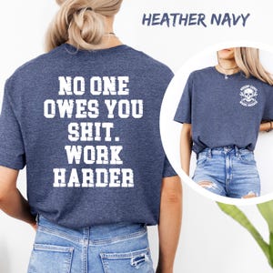 May include: Heather navy t-shirt with the text "NO ONE OWES YOU SHIT. WORK HARDER" in white block letters on the back. A smaller image of a skull with crossed wrenches and the words "NOBODY CARES WORK HARDER" is on the front.