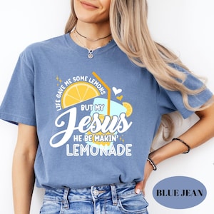 May include: Blue jean-colored t-shirt with a graphic of a lemon slice, a glass of lemonade, and the text "Life gave me some lemons but my Jesus he be makin' lemonade." The shirt has a crew neck and short sleeves.