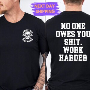 May include: Black crew neck t-shirt with white text and graphics. The front features a skull with tools and the words "NOBODY CARES WORK HARDER". The back says "NO ONE OWES YOU SHIT. WORK HARDER".