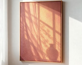 May include: A rectangular canvas wall art piece in a light wood frame, featuring a warm, terracotta-colored surface with a soft, golden-toned shadow cast across it, depicting the silhouette of a vase and vertical window pane lines.