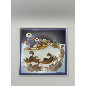 Könnte beinhalten: Quadratische Keramikfliese mit einer Winterszene mit einem Hundeschlitten. Die Illustration zeigt eine Person in einem blauen Parka, die einen Schlitten mit Passagieren lenkt, der von einem Team von Huskys über eine verschneite Landschaft gezogen wird. Die Fliese hat einen blauen Rand.