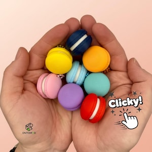 Può includere: Una collezione di macaron in miniatura colorati, gialli, arancioni, blu, verdi, viola, rosa e rossi. Ogni macaron ha una farcitura a contrasto. L'immagine include il testo "Clicky!"