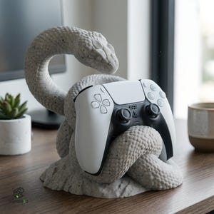 Può includere: Una scultura di serpente in cemento testurizzato grigio chiaro avvolta in una base circolare, progettata per sostenere un controller per videogiochi wireless bianco e nero. La testa del serpente è arcuata verso l'alto e il controller poggia saldamente.