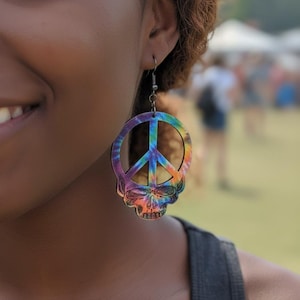 May include: Tie-dye peace sign earrings with a skull design. The earrings feature a colorful rainbow pattern and a silver hook. The peace sign is in the center of the design.