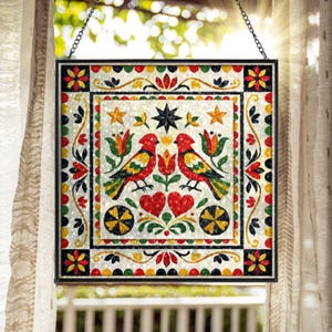 May include: A square stained glass suncatcher featuring two red birds facing each other, surrounded by floral motifs, hearts, and stars. The design uses a vibrant palette of red, yellow, green, and black, framed in a thin black metal border with a chain.