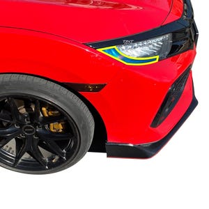 May include: A bright red car front end featuring a headlight with a yellow and blue accent decal. The headlight assembly includes the text TINT DECAL. The vehicle has a black wheel with gold brake calipers and a black front bumper lip spoiler.