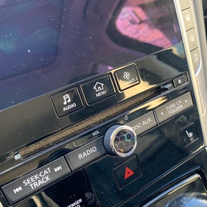 Puede incluir: Primer plano del salpicadero de un coche con una perilla negra y plateada, botones etiquetados como "Audio", "Menú", "Seek-Cat Track", "Radio", "Disc-Aux", "Tune-Ch Folder" y "Passenger Air Bag".