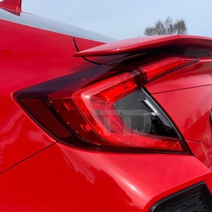 May include: A red car with a black rear spoiler and a red taillight. The taillight has a clear lens with a black housing.
