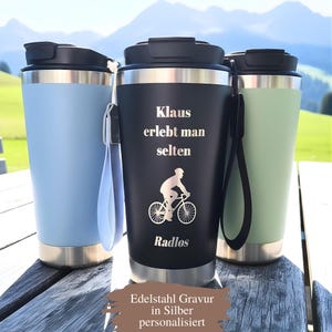 Könnte beinhalten: Drei Edelstahl-Reisebecher in Hellblau, Schwarz und Grün. Der schwarze Becher zeigt eine Radfahrer-Grafik und den Text "Klaus erlebt man selten" und "Radlos". Die Becher haben schwarze Deckel und silberne Böden, mit einem Band. Berge im Hintergrund.