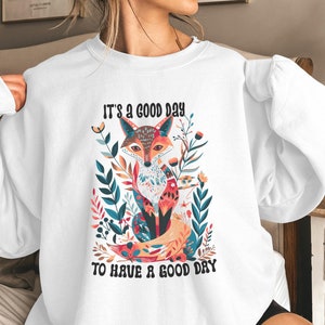 Könnte beinhalten: Weißer Pullover mit einer bunten Fuchsillustration und dem Text "Es ist ein guter Tag, um einen guten Tag zu haben".