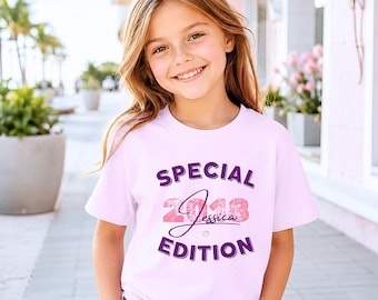 May include: A light pink short-sleeved t-shirt featuring the purple text SPECIAL EDITION, the pink glittery number 2018, and the name Jessica in cursive script with a small heart icon centered on the front of the garment.