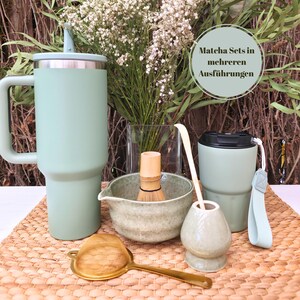 Könnte beinhalten: Ein Matcha-Tee-Set in Grüntönen, darunter ein großer Becher mit Griff, ein Schneebesen, eine Schüssel, ein Löffel und eine kleine Tasse. Ein goldfarbenes Teesieb ist ebenfalls vorhanden. Der Text "Matcha Sets in mehreren Ausführungen" ist sichtbar.