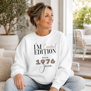 Könnte beinhalten: Ein weißes Sweatshirt mit Rundhalsausschnitt und dem schwarzen sowie taupefarbenen Text I'M Limited EDITION Born in 1976 Jana mit einem kleinen Herzsymbol. Das Design ist mittig auf der Brust des langärmeligen Pullovers platziert, der gerippte Bündchen hat.