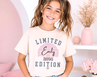May include: A cream-colored short-sleeve t-shirt featuring the text LIMITED EDITION in dark blue block letters, with the name Emily in black script over a pink semi-circle graphic and the year 2014 printed below, finished with a small heart icon.