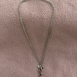 May include: A silver-toned necklace with a Minnie Mouse pendant. The pendant features Minnie's iconic bow with pink accents. The chain is delicate and hangs on a pink background. A small, round charm is near the clasp.