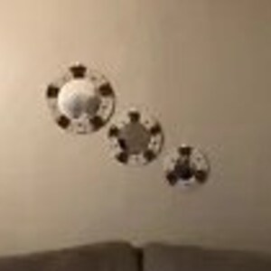 May include: Three round decorative mirrors with a crown design are mounted on a beige wall. The mirrors vary in size, with the largest in the center. The crowns are gold-colored, and the mirrors have a reflective surface.