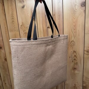 May include: A brown tote bag with black straps. The bag is made of a woven fabric and has a simple design.