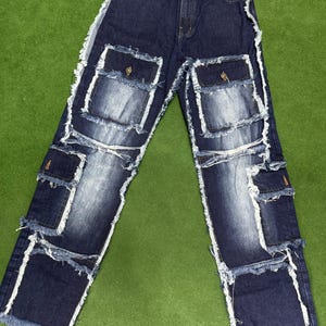 Peut inclure: Jean en denim bleu fonc&eacute; avec plusieurs poches plaqu&eacute;es et des bords blancs effiloch&eacute;s. Le jean a une conception classique &agrave; cinq poches avec des poches suppl&eacute;mentaires de style cargo. Le denim a un effet d&eacute;lav&eacute; et les bords sont effiloch&eacute;s.
