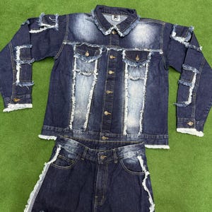 Peut inclure: Ensemble en jean deux pi&egrave;ces compos&eacute; d'une veste et d'un short. La veste en jean bleu fonc&eacute; a une fermeture boutonn&eacute;e, des poches poitrine et des d&eacute;tails d&eacute;chir&eacute;s. Le short a des accents d&eacute;chir&eacute;s assortis. L'ensemble est pr&eacute;sent&eacute; sur une surface verte.
