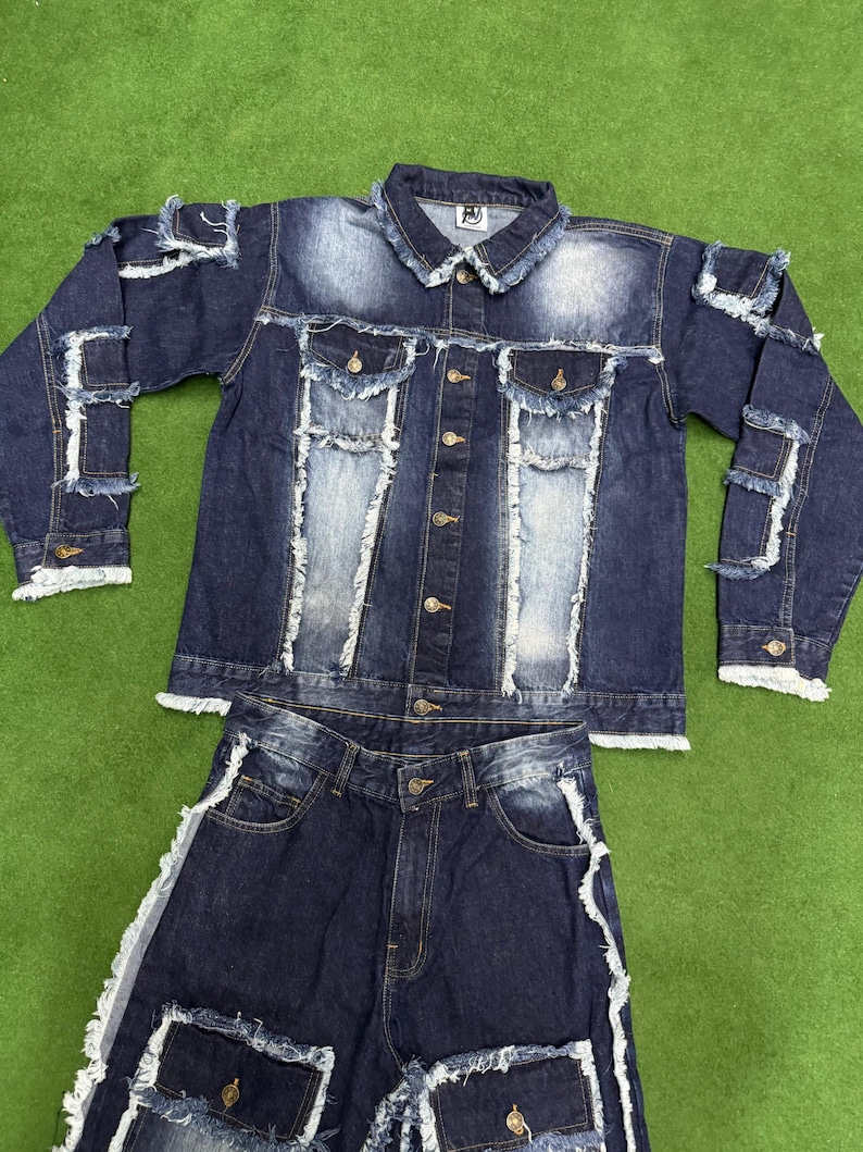 Peut inclure: Ensemble en jean deux pi&egrave;ces compos&eacute; d'une veste et d'un short. La veste en jean bleu fonc&eacute; a une fermeture boutonn&eacute;e, des poches poitrine et des d&eacute;tails d&eacute;chir&eacute;s. Le short a des accents d&eacute;chir&eacute;s assortis. L'ensemble est pr&eacute;sent&eacute; sur une surface verte.