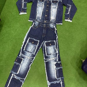Peut inclure: Un ensemble veste et jean en denim. Le denim bleu fonc&eacute; pr&eacute;sente des patchs d&eacute;lav&eacute;s bleu clair et des bords effiloch&eacute;s. La veste a une fermeture boutonn&eacute;e et le jean des poches cargo.