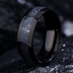May include: A black tungsten carbide ring with a grey inlay. The ring has a polished finish and a comfortable fit.