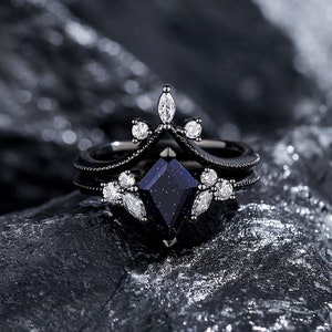 May include: Black ring set with a large blue gemstone and smaller clear gemstones. The ring is made of black metal and has a delicate design.