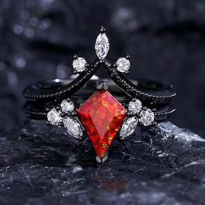 May include: Black ring set with a large red gemstone and smaller white gemstones. The ring has a crown-like design.