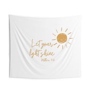 Puede incluir: Tapiz blanco con un sol dorado y el texto "Let your light shine" y "Matthew 5:16".