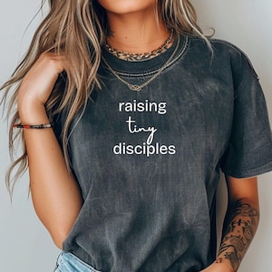 May include: A dark gray t-shirt with the text "raising tiny disciples" printed in white.