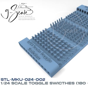 May include: A blue plastic model kit of 180 1/24 scale toggle switches. The kit includes a base with the text "1/24 Scale Toggle Switches", "Guard Down", "Guard Up", and "No Guard".