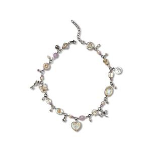 May include: A charm necklace featuring a dark metal chain adorned with various small pendants including a heart, a dragonfly, a key, a button, and several floral-shaped charms, interspersed with small light purple and clear glass beads.