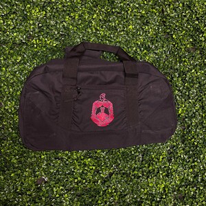 May include: Black duffel bag with a red embroidered Greek letter fraternity crest.
